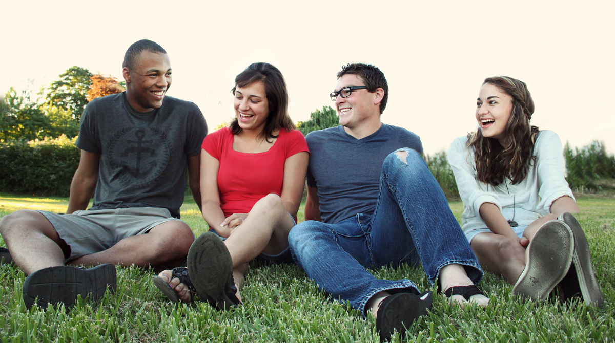 a group of 2 girls and 2 men sitting on the grass